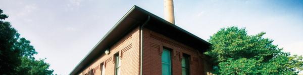 A small red brick building with a smoke stack on beautiful sunny day.